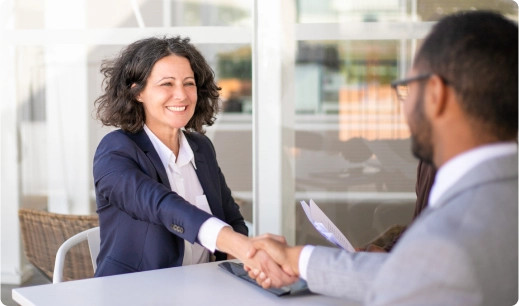Woman facing camera shaking hands with man across a table