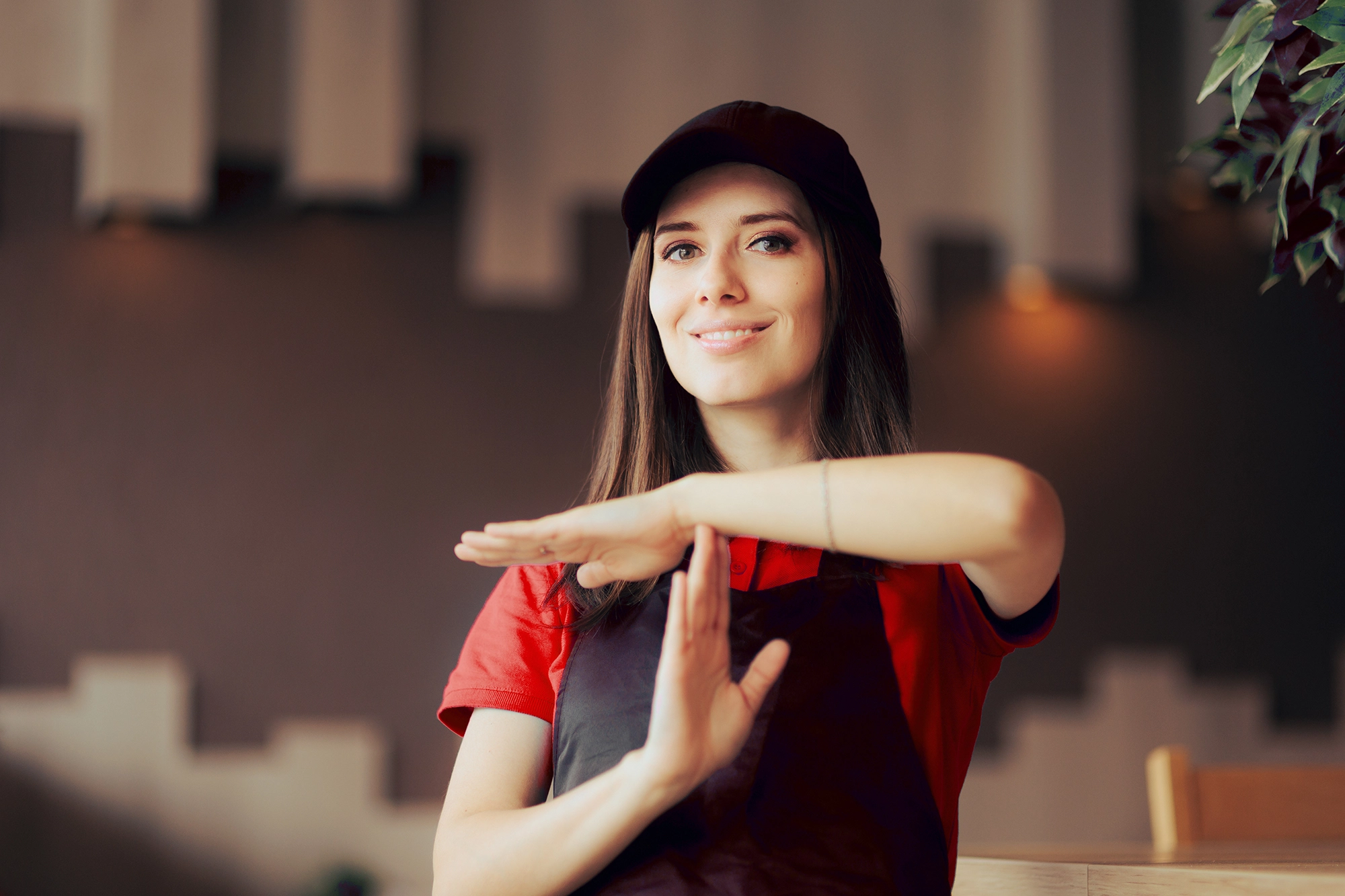 Fast food worker in black apron and red shirt holds arms in a T position, indicating a time out or break