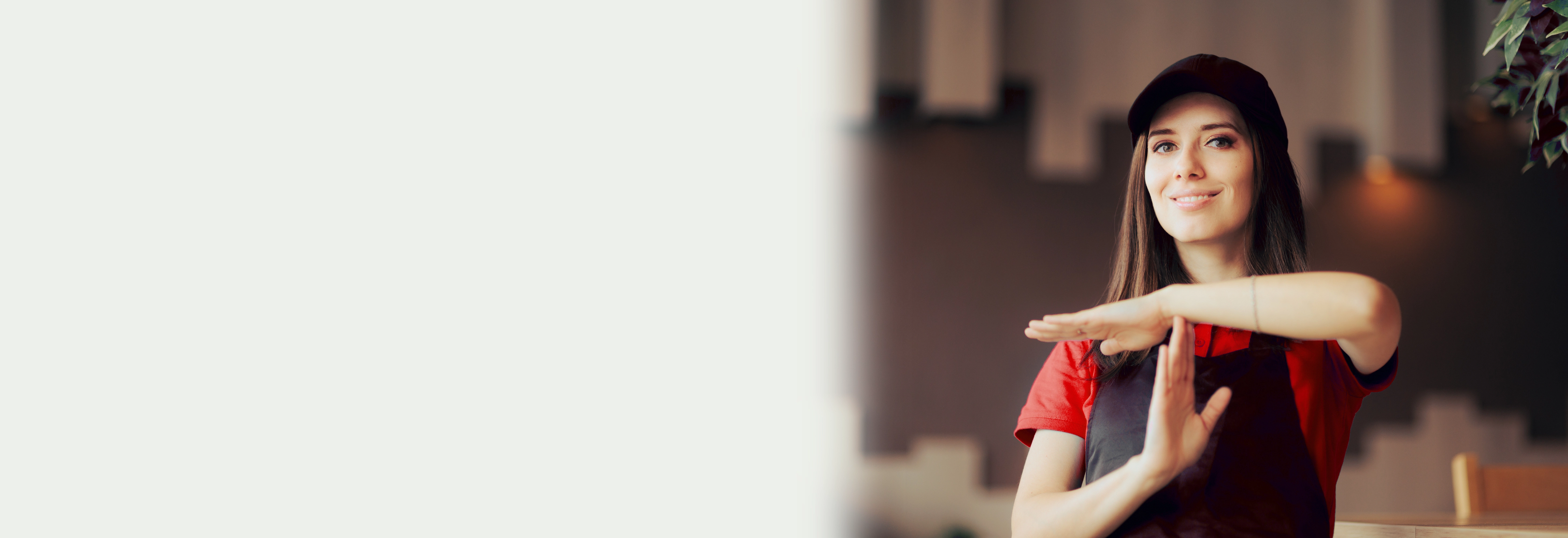 Fast food worker in black apron and red shirt holds arms in a T position, indicating a time out or break
