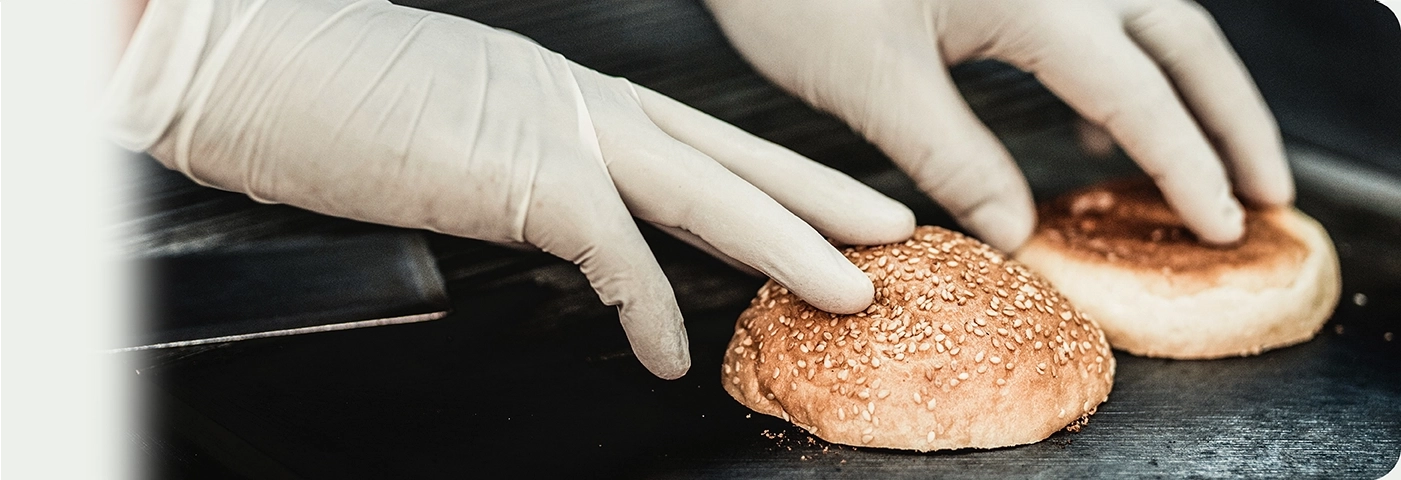 Gloved hands placing burger buns on a grill