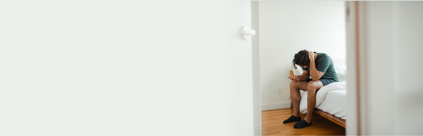 Desktop header. Man sitting on bed holding phone looking stressed